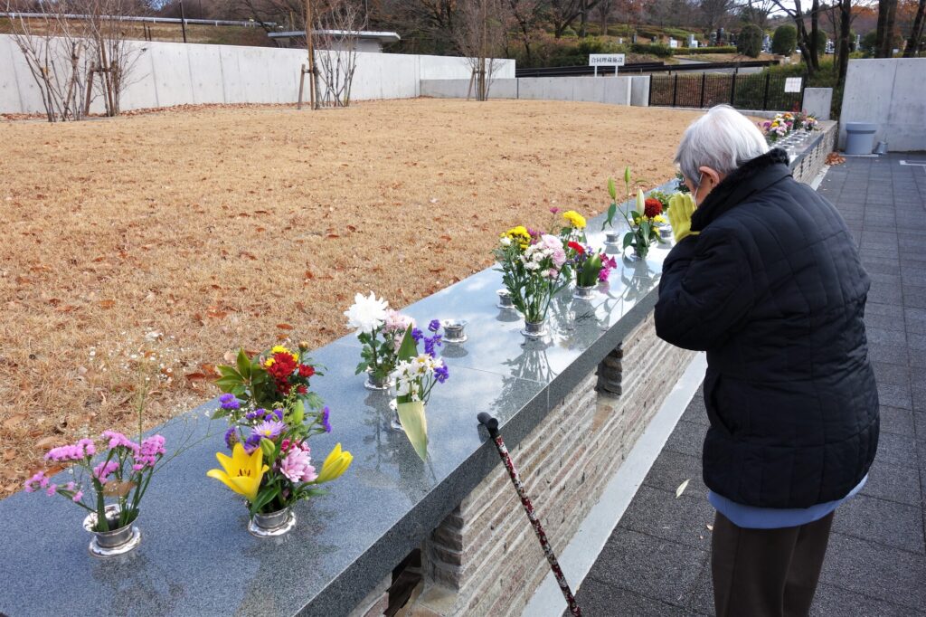 花が供えられた墓所で手を合わせる参拝者